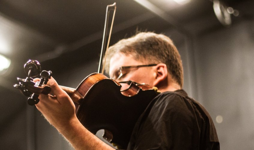 A fiddler plays live music at a contra dance. Photo by Sam Whited, used here under Creative Commons license with thanks.